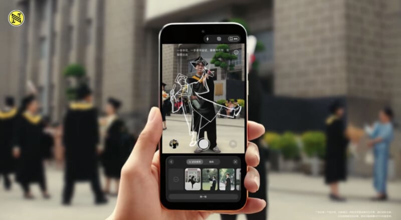A person holds a smartphone showing an augmented reality outline of a graduate in cap and gown. In the background, people in graduation attire stand outside a building.