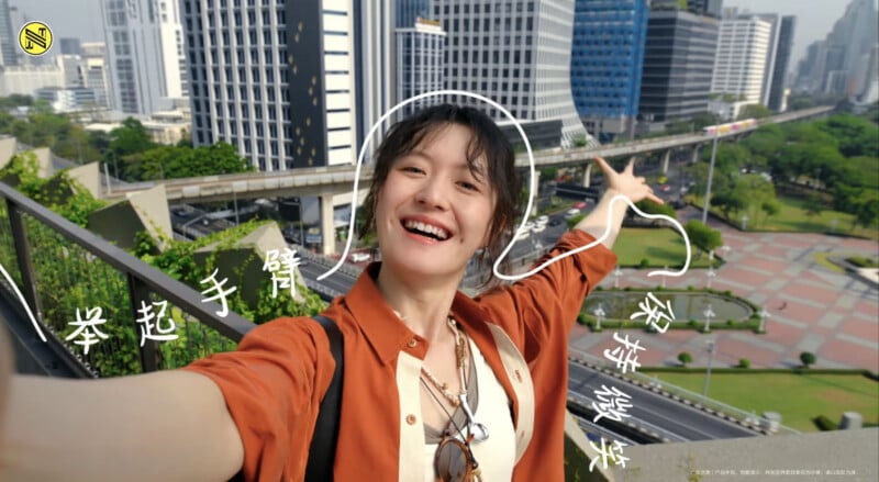 A smiling person takes a selfie on a city balcony, pointing toward skyscrapers and a green park. White doodles and Chinese characters decorate the image, adding a playful touch.