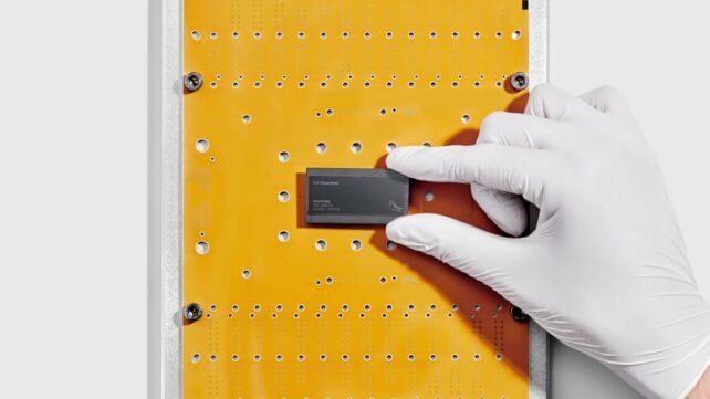 White gloved hand hold black, rectangular chip on yellow background.