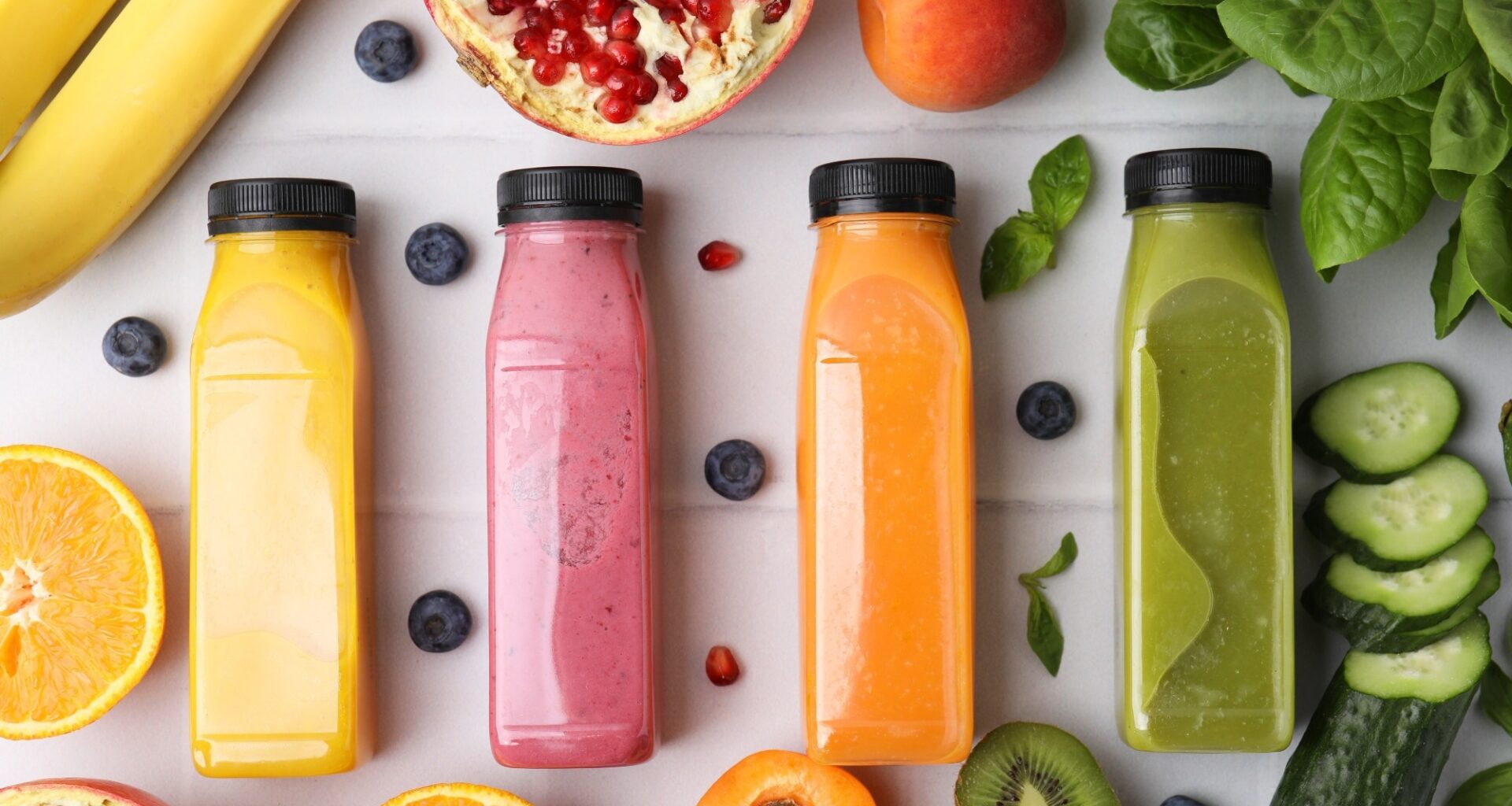 Glass bottles of tasty smoothies and different products on white tiled table, flat lay