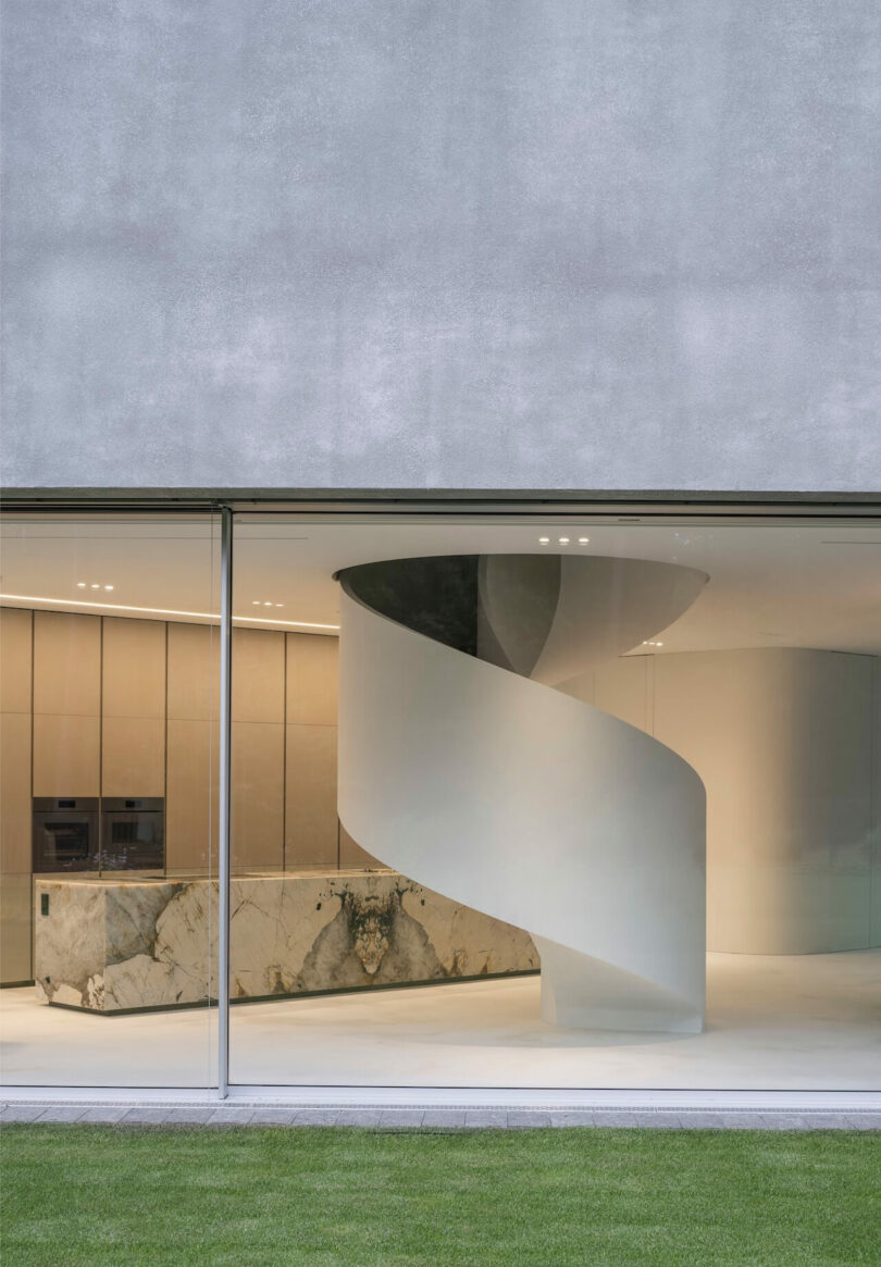 A modern interior by KWK Promes with a large glass window, white spiral staircase, light wooden cabinetry, and a marble kitchen island. Green grass is visible outside.