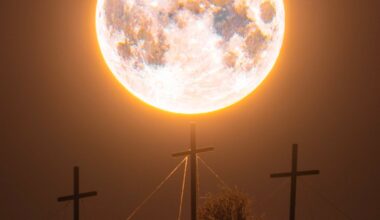 A large, bright full moon appears to rest atop a central cross, with two other crosses nearby, all silhouetted against the night sky. The scene evokes a powerful, ethereal atmosphere.
