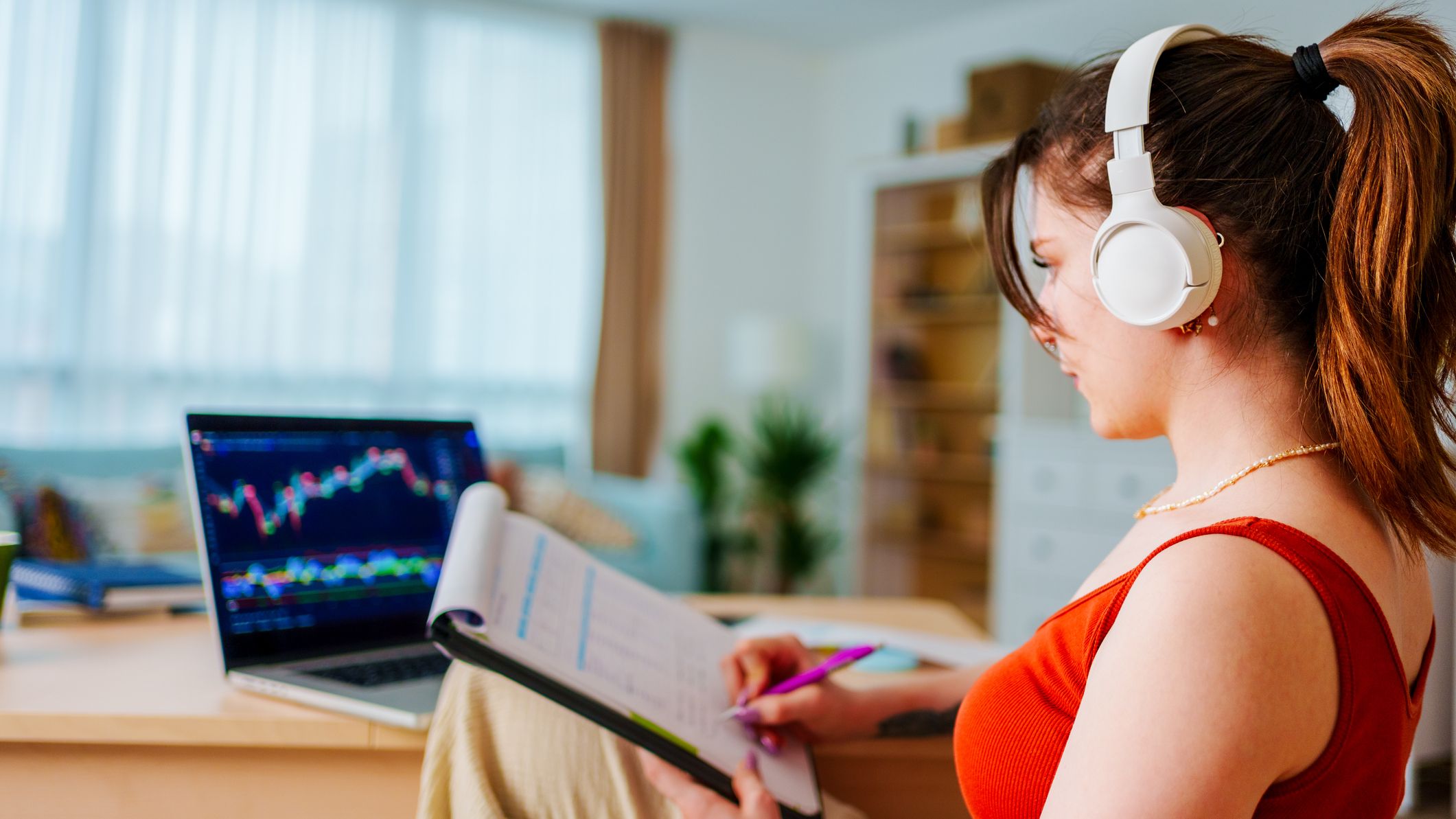 Young Businesswoman with Headphones checking Bitcoin or stock exchange price chart on digital exchange on a laptop monitor computer at her desk at home