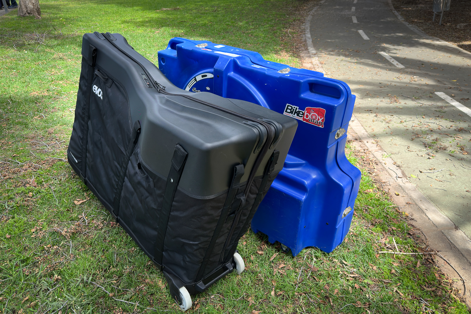 a black bike bag and a blue bike box next to a green cycle path