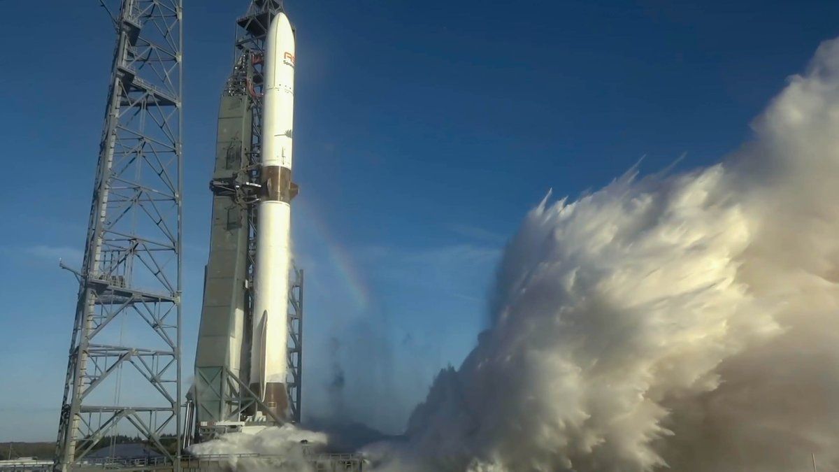 a large white rocket conducts an engine test on the pad beneath a blue sky