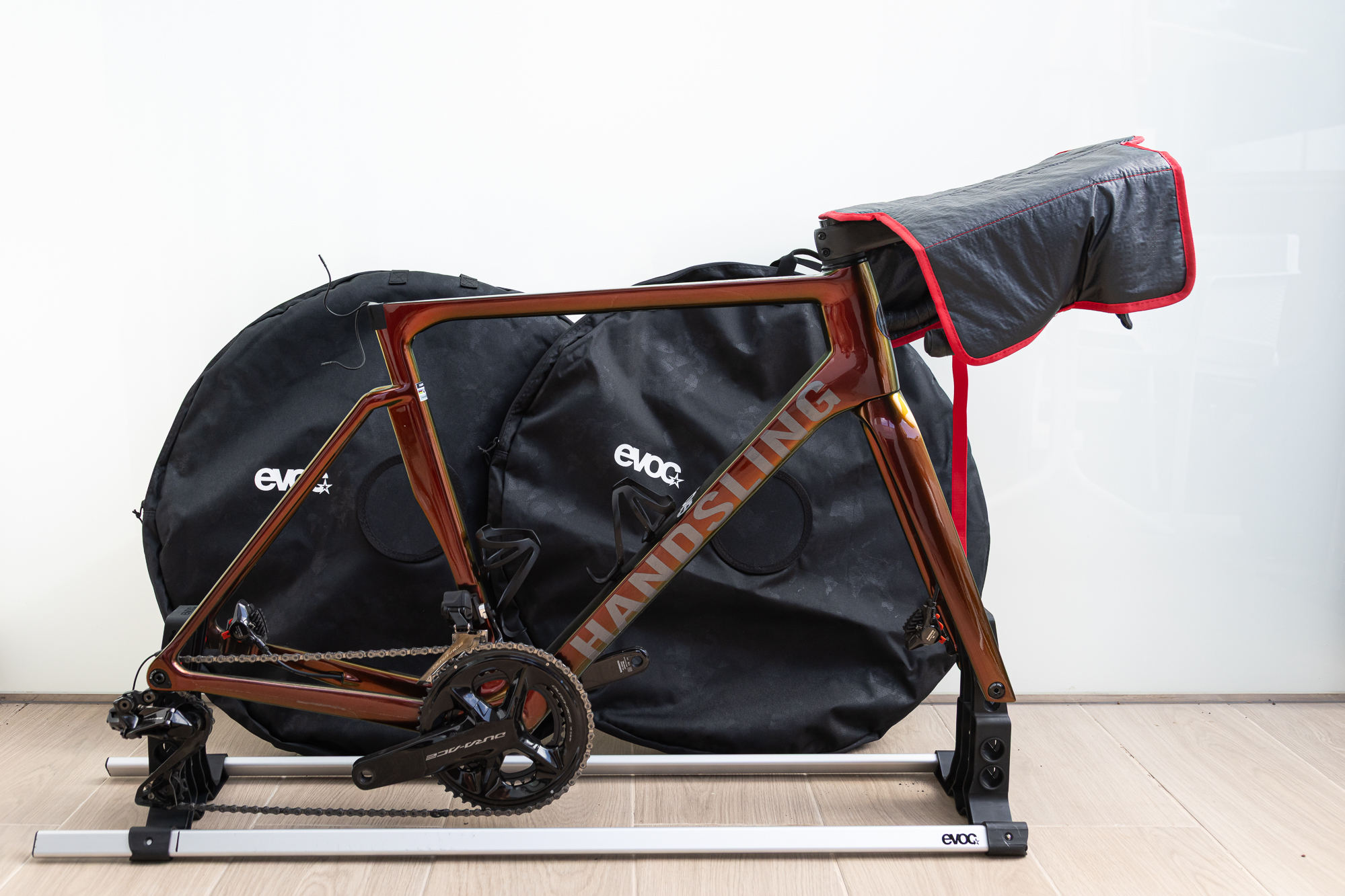 An orange bike frame mounted on a simple metal frame with wheels in bags behind it