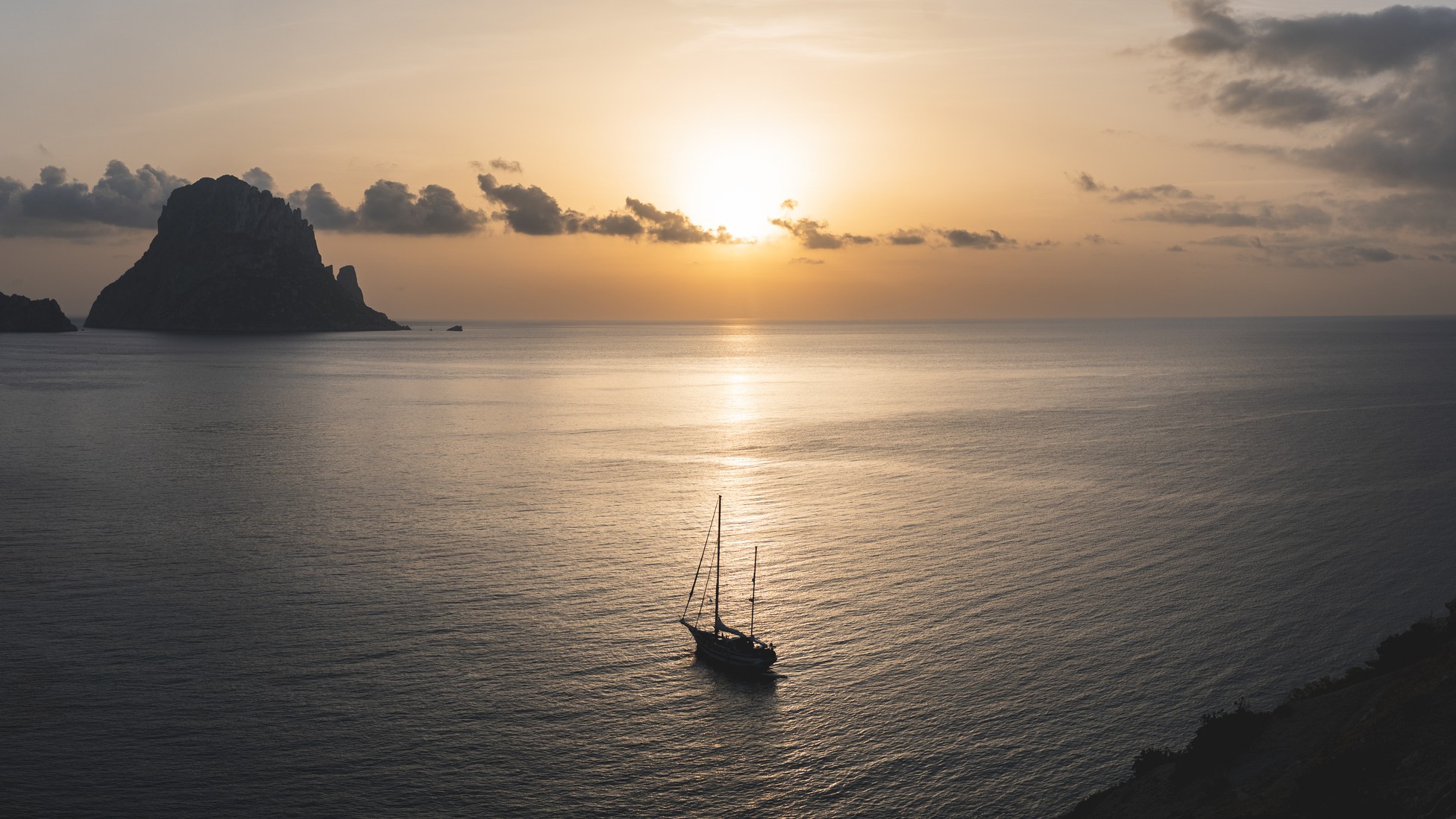 a sail boat on calm water and the sun shining in the distance.