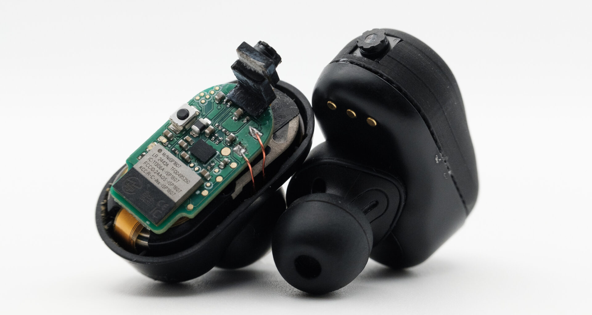 Two black earbuds: one with the casing removed exposing a computer chip and tiny camera.