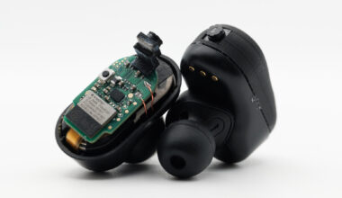 Two black earbuds: one with the casing removed exposing a computer chip and tiny camera.