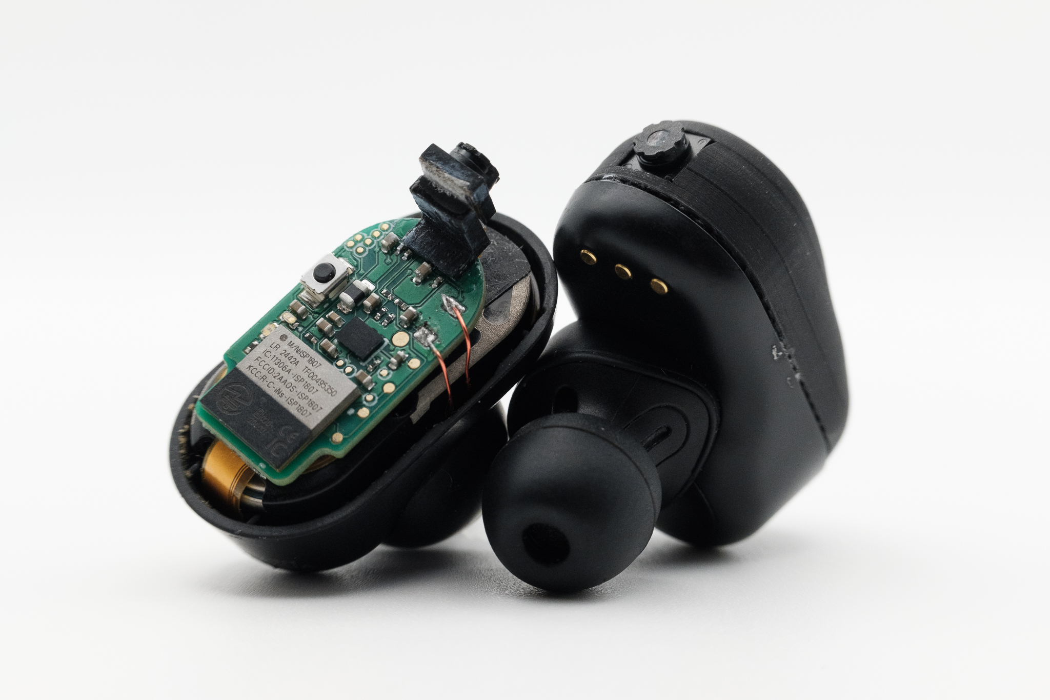 Two black earbuds: one with the casing removed exposing a computer chip and tiny camera.