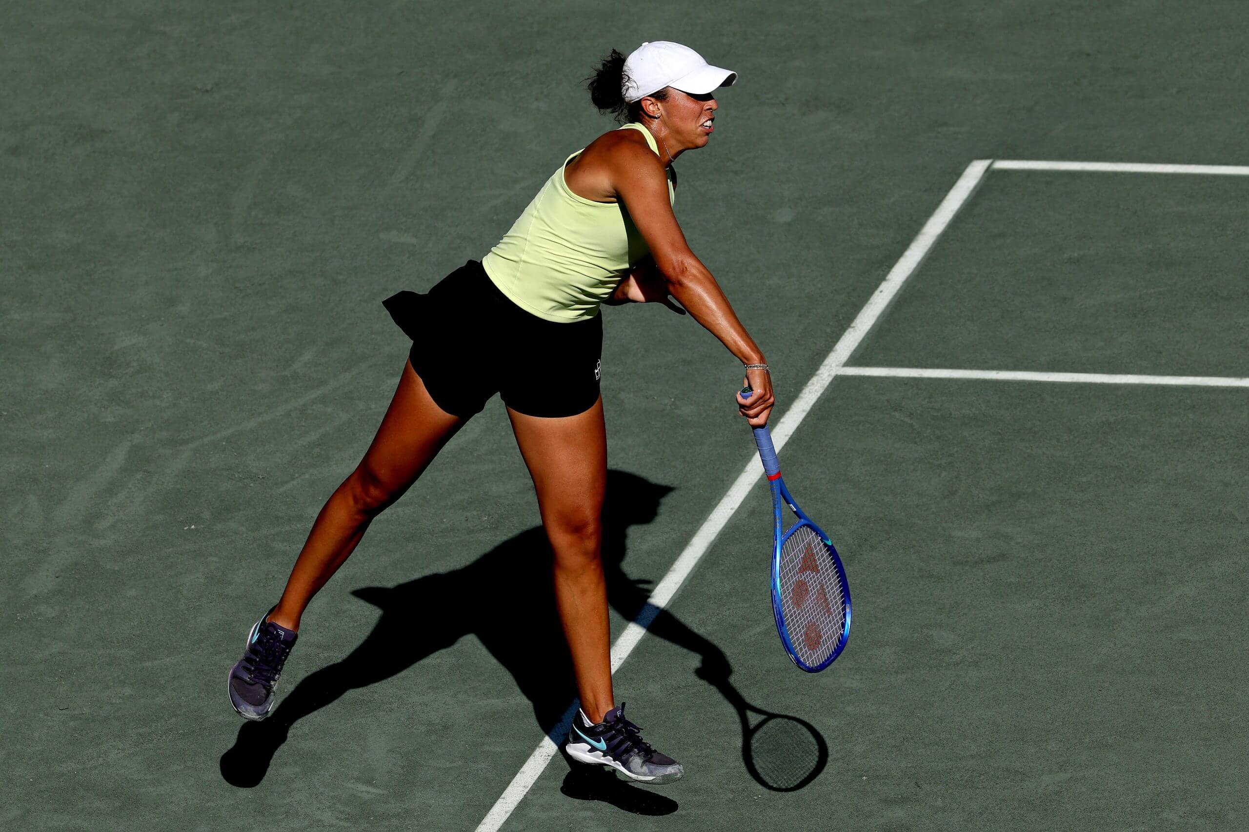 Madison Keys follows through on a serve in mid-air on a green tennis court.