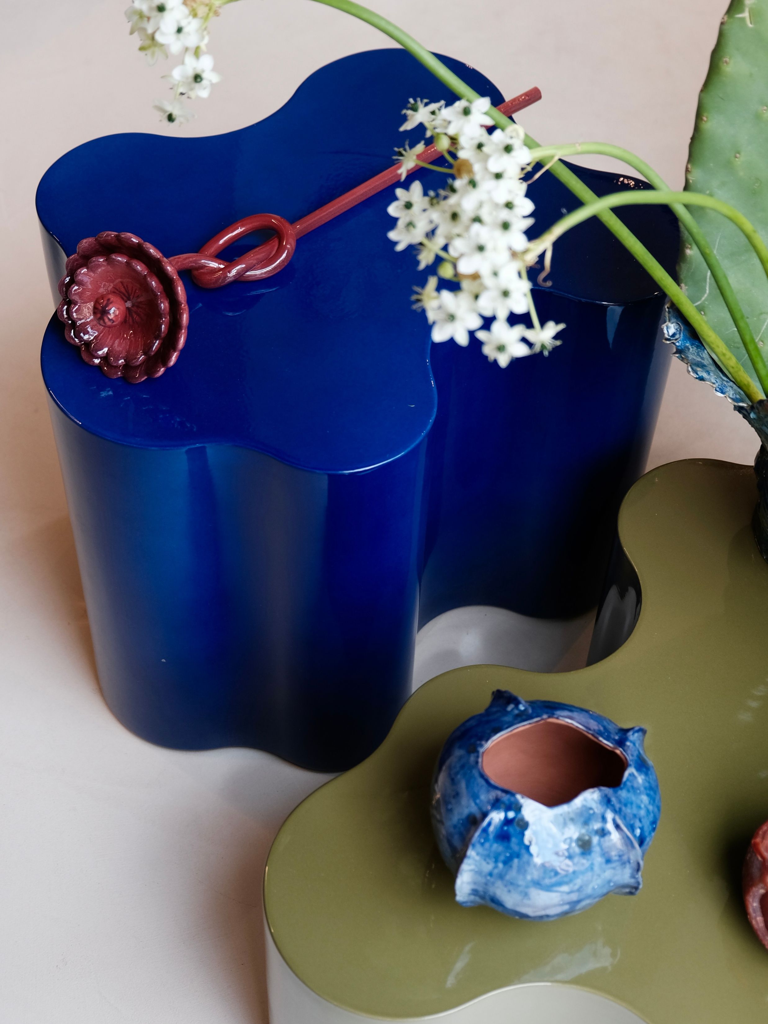a blue wavy side table with a ceramic flower on top