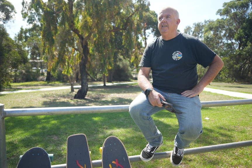 A man sits on a fence alongside skateboards.