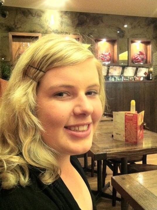 A smiling young blonde woman in a restaurant.