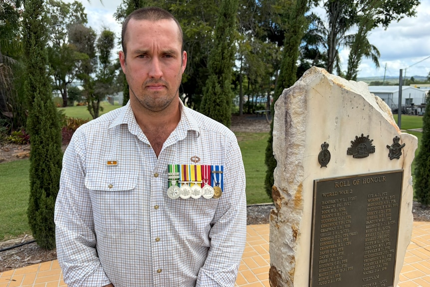 A man with a row of medals on his chest standing next to a war monument
