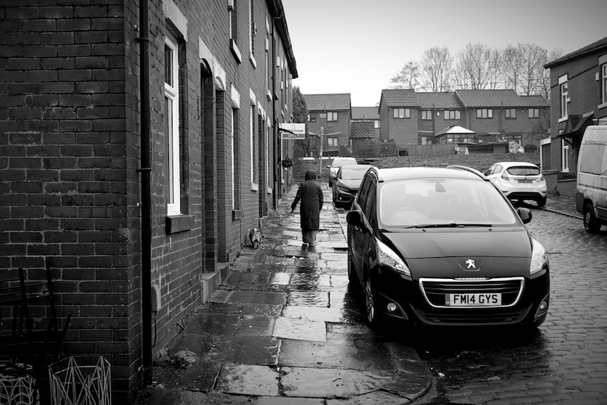 A person in a black puffer jacket walks down a rainy street.