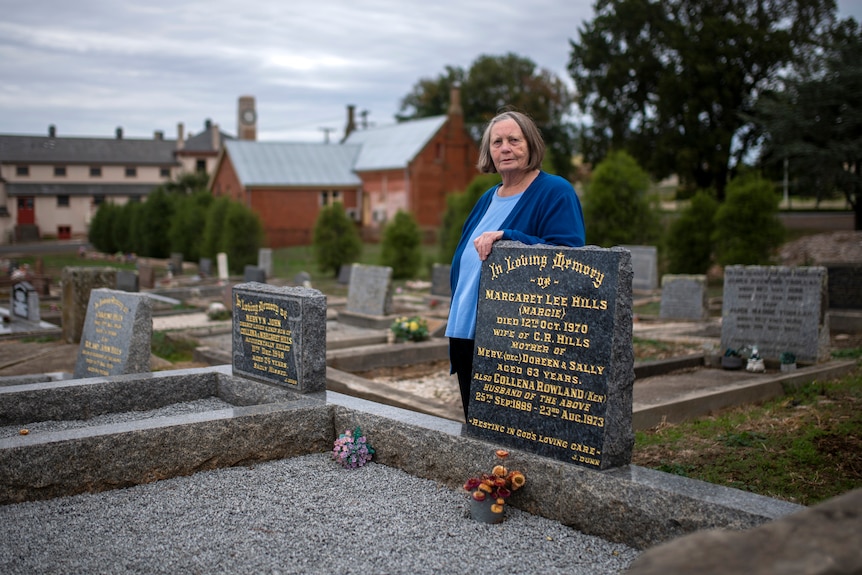 A woman in a blue cardigan stands in a cemetery on a cloudy day.