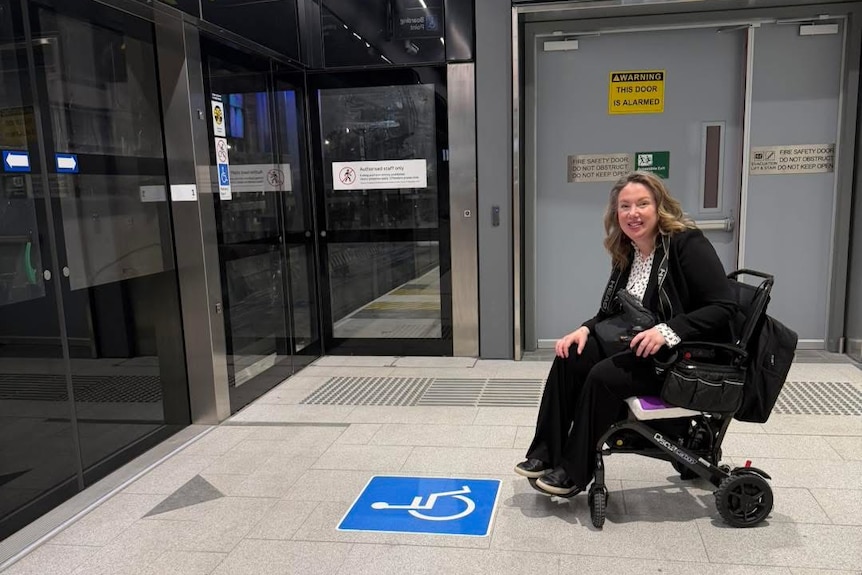 A smiling, middle-aged woman in a wheelchair at a train station.
