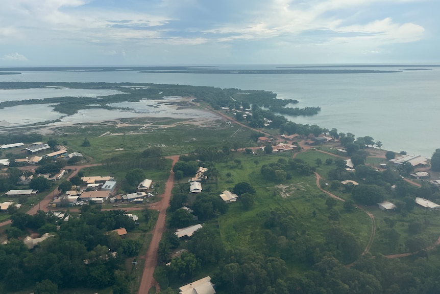A drone photo of a small coastal community, with houses lined up either side of a red dirt road.