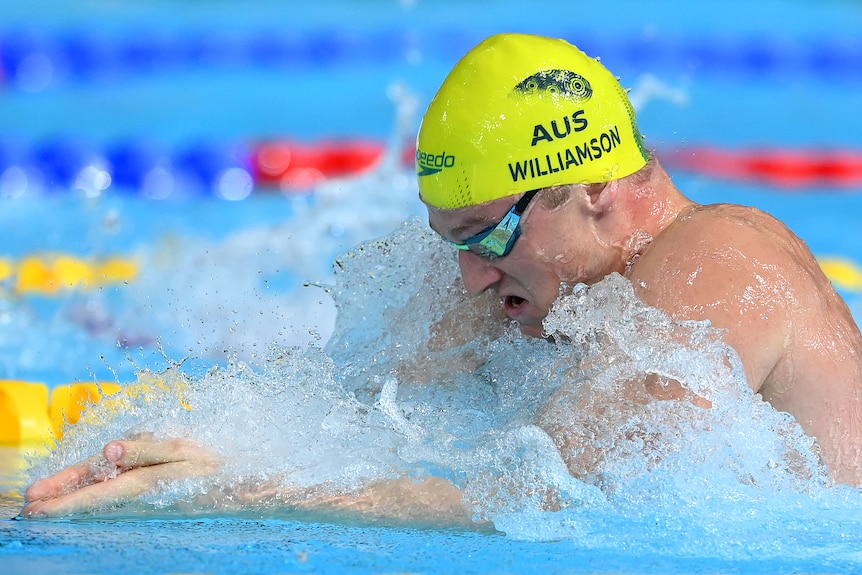 Sam Williamson swims in a yellow AUS hat