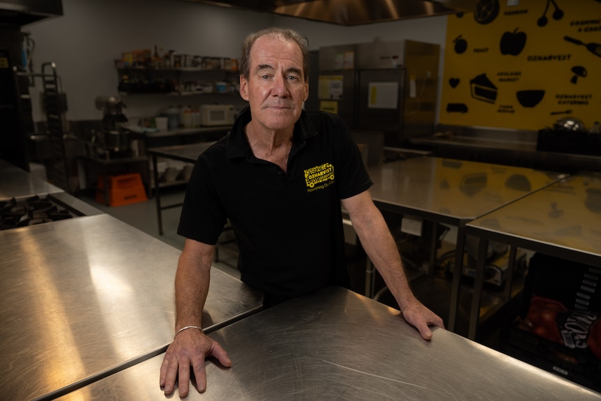 A man stretches both arms out on a stainless steel commercial countertop in a large kitchen