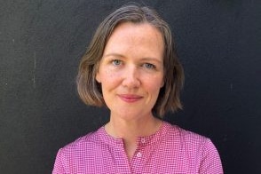 a woman is smiling and wearing a pink shirt.