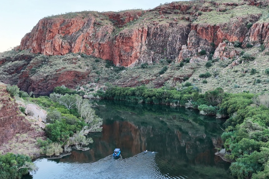 swimmer and bot on a river surrounded by red rock cliffs