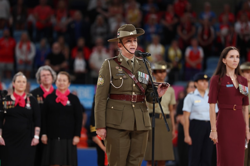 A female army officer reads The Ode in front of a packed stadium