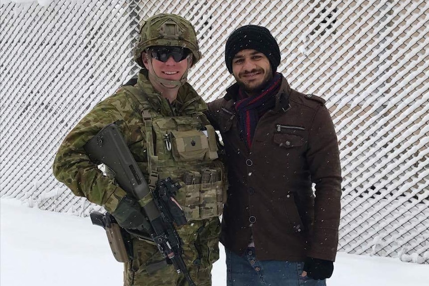 Two men, one in an army uniform, stand and smile in the snow.