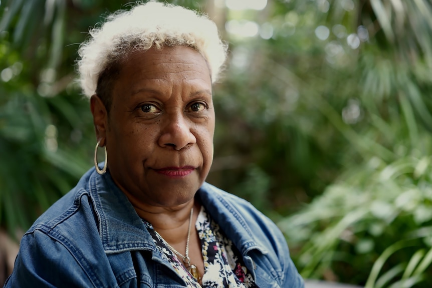 Gail looks at the camera, dense green trees in the background