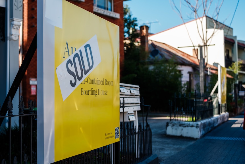 Yellow sign in front of properties with a big 'Sold' on it.