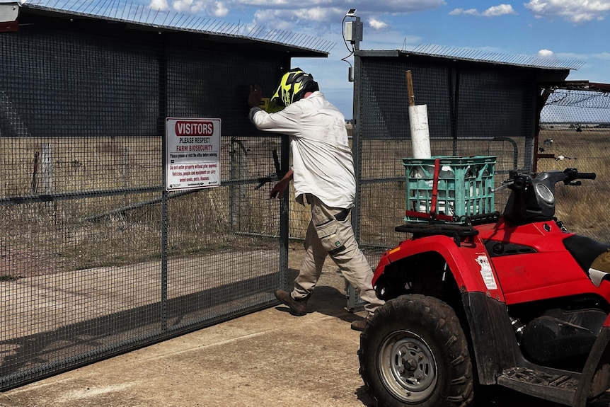 Man pushing a gate open with a tractor behind him.