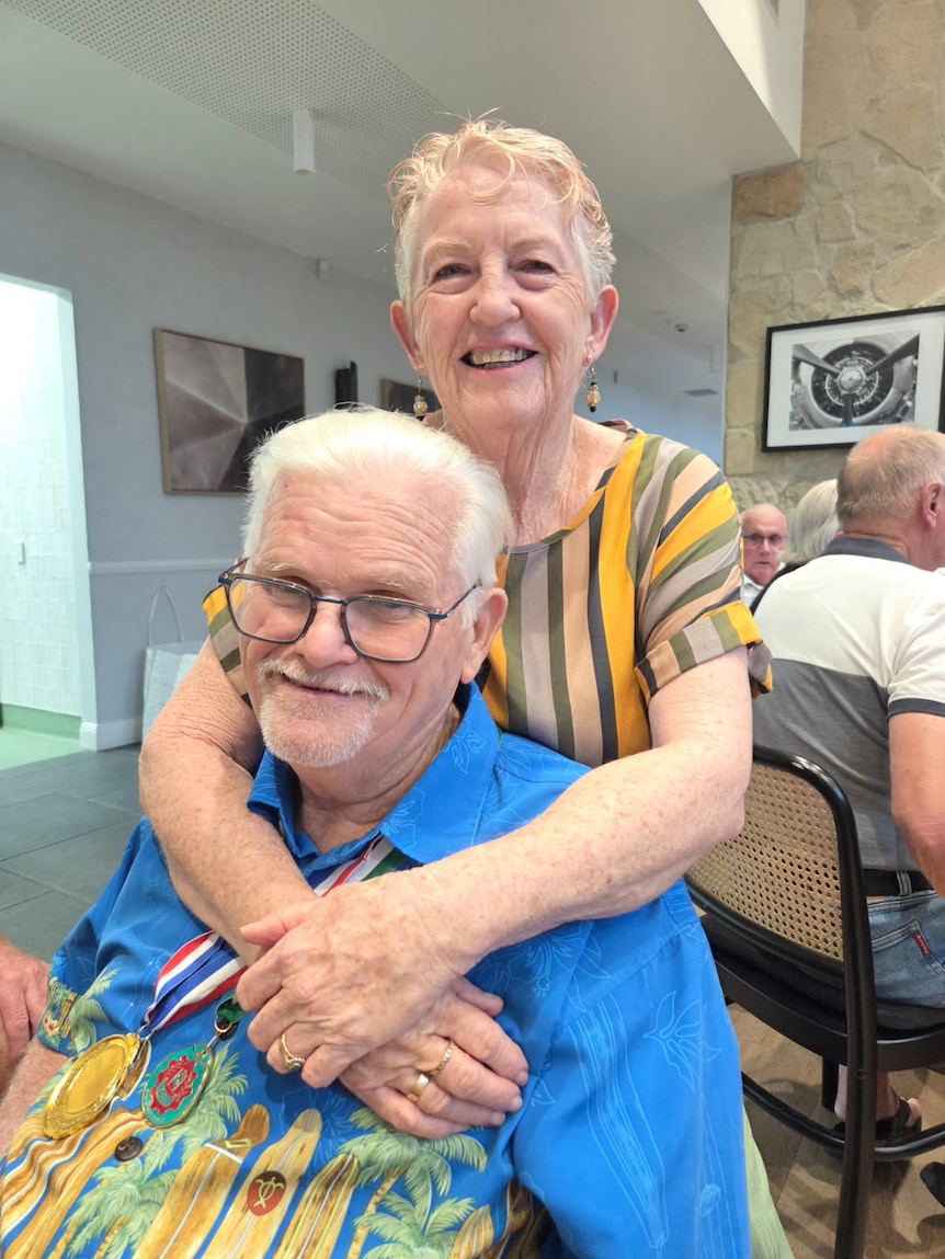  A happy older couple smile at the camera from a dining table.