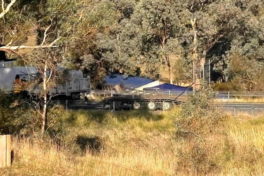 A grassy landscape with a road and a truck on its side