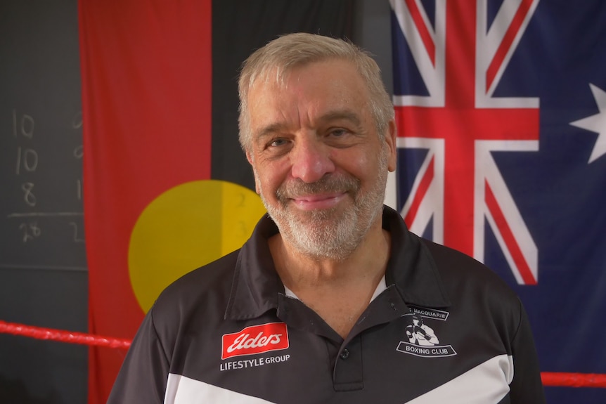 Man smiling in front of the Aboriginal and Australian flags