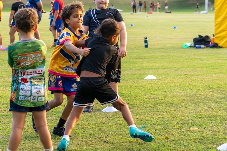 A young boy tackles another young boy during rugby league training.