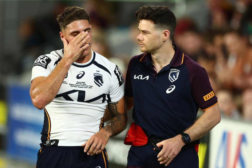 A rugby league player in white holds his face and walks off