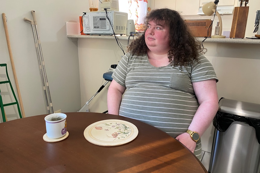 A woman drinks a cup of tea at her dining table.