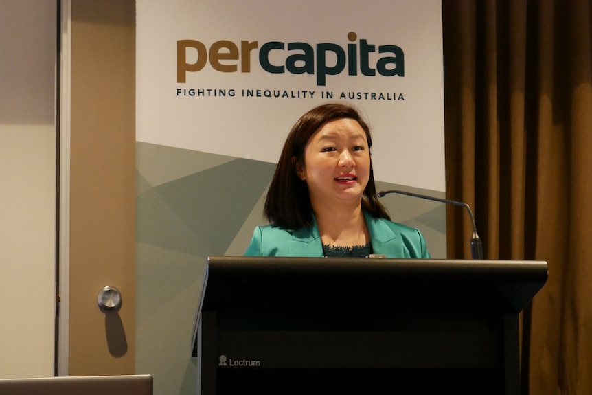 A woman in a bright green suit stands in front of a lectern speaking.
