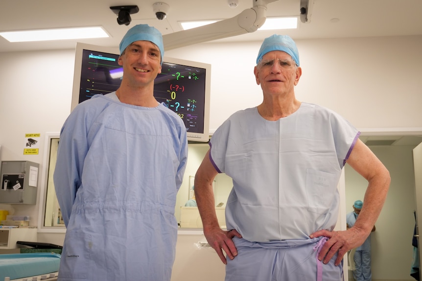 Two men in blue hospital scrubs smiling, in operating theatre. 
