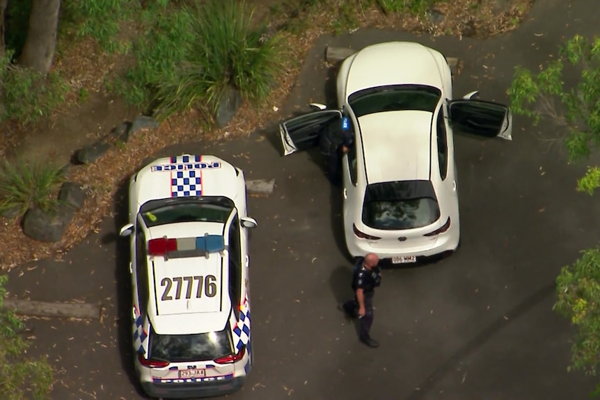A view from above of a Queensland Police car and a white car parked on a road with an officer standing behind on of the cars.
