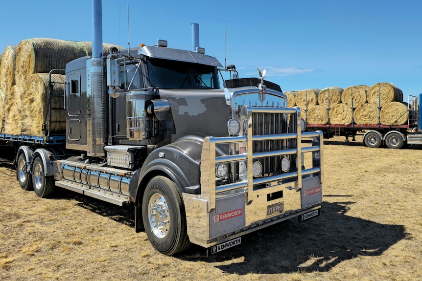 Two trucks hauling bales of hay.
