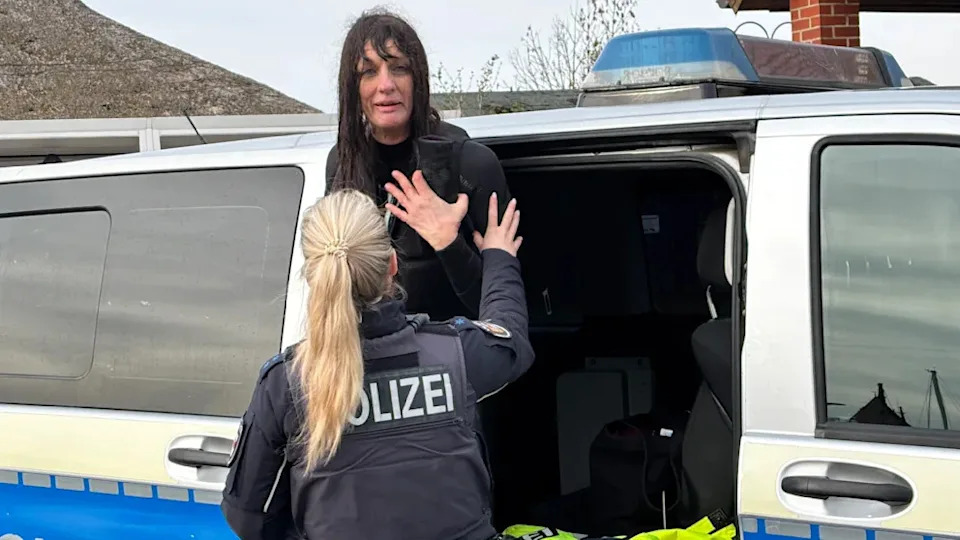 Nicola (58) from Munich is soaking wet after attempting to reach the whale. She's being pushed inside a police van.