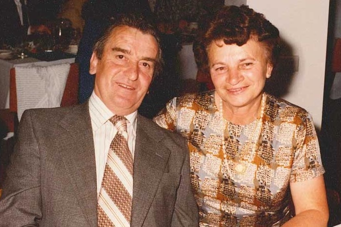 An old photo of a man and a woman, nicely dressed, sitting next to each other smiling.