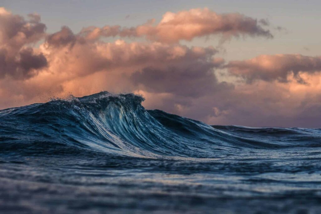 Ocean wave at sunset with dramatic clouds, showcasing natural marine beauty.
