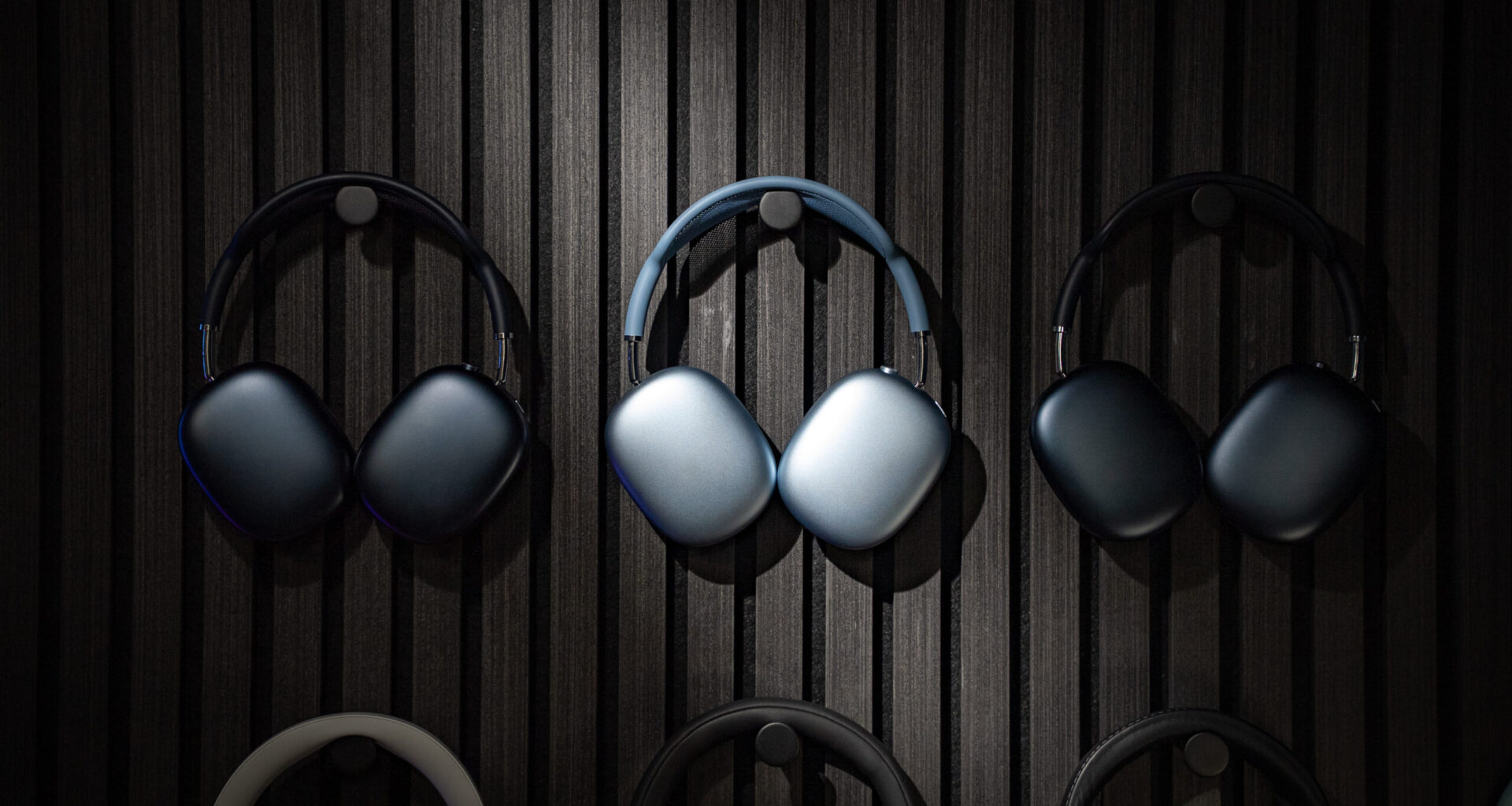 Apple AirPods Max 2 headphones hanging on a wall alongside two older generation AirPods Max headphones.