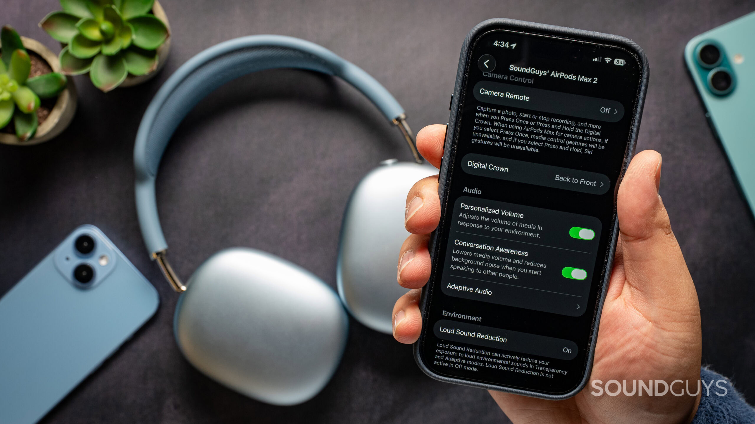 apple airpods max 2 personalized volume conversation awareness Apple AirPods Max 2 headphones on table with iPhone 17 Pro in front showing different software features.