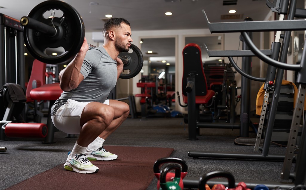Man performing barbell squats in a gym.