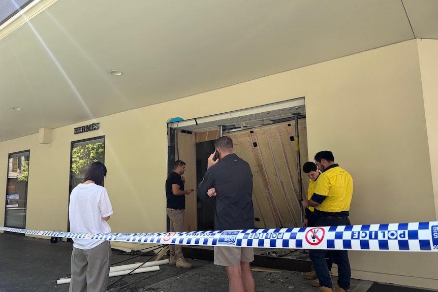 Police tape in front of a store with a smashed in wooden door.