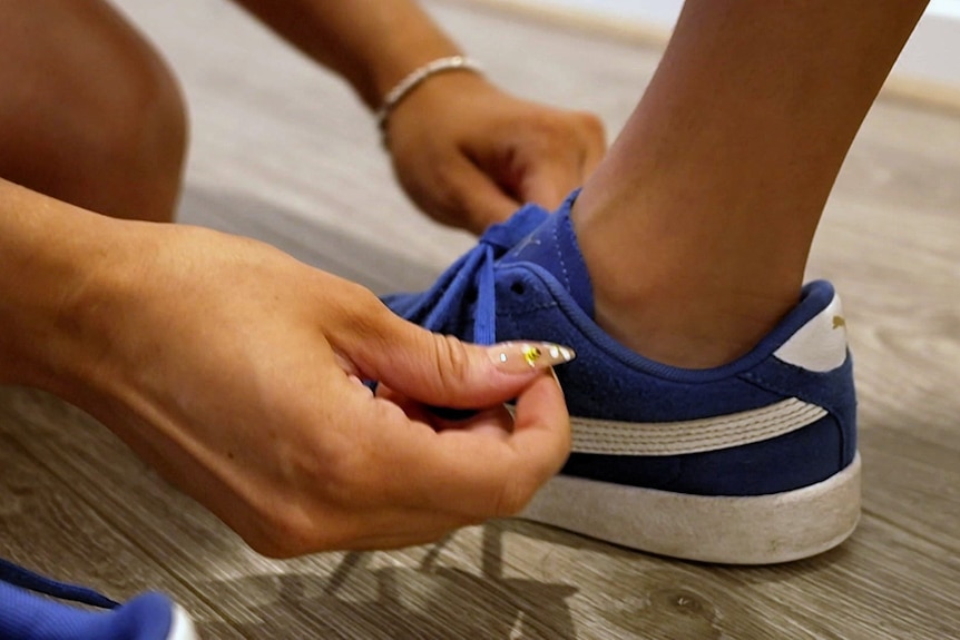 A close up of an adult woman's hands tying a child's blue sneakers